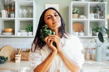 Attractive young woman stands in the kitchen and holds a bunch of fresh mint