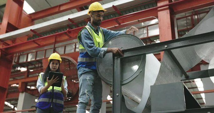 team of technicians is inspecting steel sheet production machinery in a large factory. An operator is inspecting a machine using a tablet. Control the factory production line. Concept teamwork