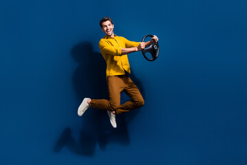 Fototapeta na wymiar Full length photo of nice young male jumping hold steering wheel dressed stylish yellow garment isolated on dark blue color background