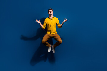 Fototapeta na wymiar Full size photo of attractive young man jumping meditate closed eyes dressed stylish yellow clothes isolated on dark blue color background