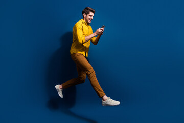 Fototapeta premium Full length photo of nice young male running hold telephone dressed stylish yellow garment isolated on dark blue color background
