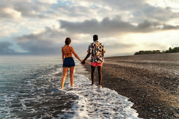 Romantic Multiethnic Couple Walking on Beach at Sunset