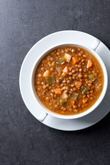 Lentil soup with vegetables in bowl on black background. 