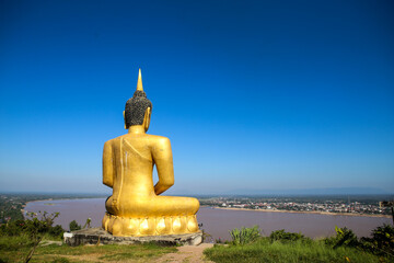 The big golden Buddha statue of Phu Salao temple with Mekong River flows through the Pakse city in beautiful sunset moment at Pakse, Laos