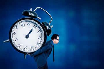Side view of young handsome man carrying huge alarm clock on his back