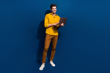 Full length photo of nice young male hold netbook working manager dressed stylish yellow garment isolated on dark blue color background