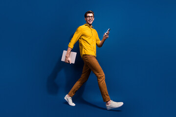 Fototapeta na wymiar Full body photo of attractive young guy walk netbook device marketer dressed stylish yellow clothes isolated on dark blue color background