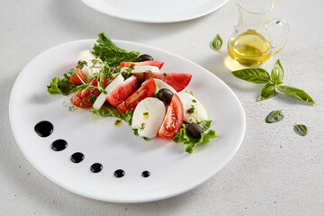 Classic Caprese salad with ripe tomatoes, mozzarella, and olives, garnished with fresh basil. Suitable for Italian cuisine promotions and cookbooks