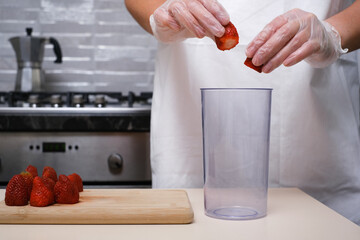 female cook putting strawberries into blender bowl