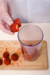 female cook putting strawberries into blender bowl