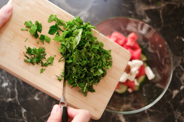 woman adding chopped greens to vegetable salad close-up