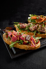 Gourmet bruschetta set with salmon, roast beef, and tuna on a black plate, side angle view