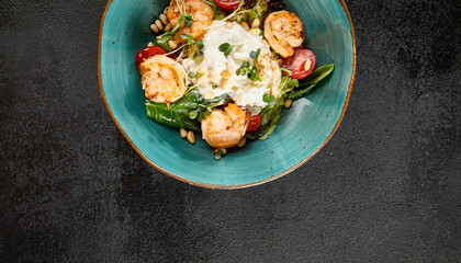 Overhead view of a salad with grilled shrimp and stracciatella cheese, mixed greens, and cherry tomatoes in a turquoise bowl