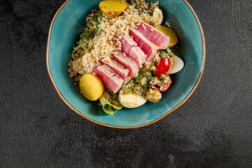 Top view of a quinoa bowl with medium-seared tuna, mixed vegetables, and a lemon wedge, served in a turquoise ceramic dish