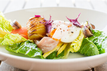 Niçoise salad with lettuce, mackerel, anchovies, roasted butter beans, baby potatoes and a poached egg on a white plate in restaurant