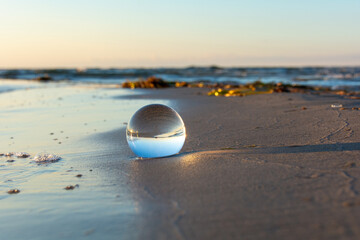 Beach and sea reflected in a sphere lying in the sand in the waves