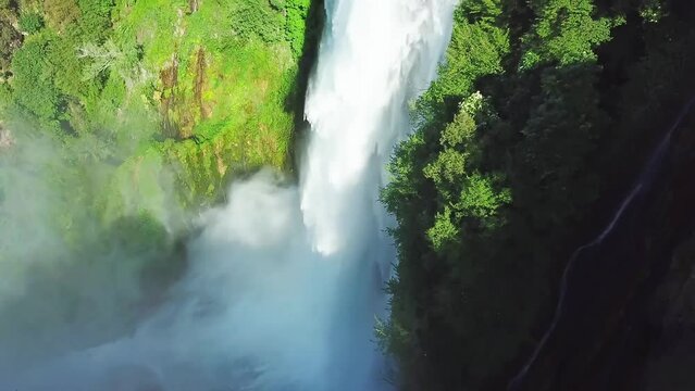 Aerial view of the majestic, roaring white waterfall rushing down from the mountain top