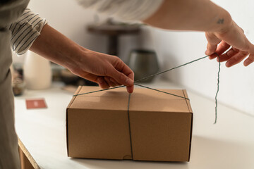 Close-up of hands tying green twine around a cardboard box on a craft table.