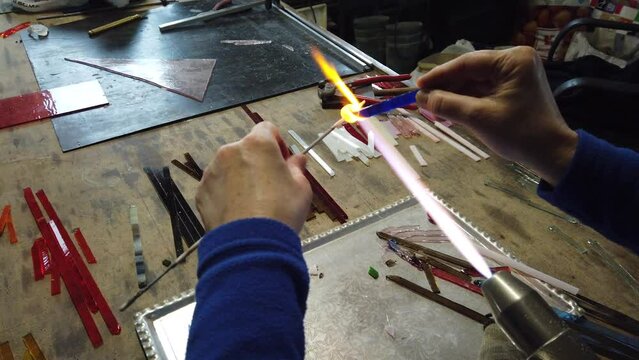 
1603, 1604, 1605, 1606, 1607, 1608, 1609                      Close up of artist hands creating glass pendant with lampworking technique. Shaping glass with flame making jewelry using gas burner