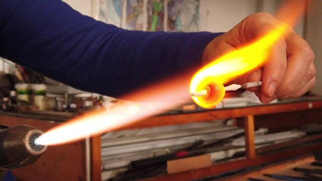 Slow motion view of artist hands creating glass pendant with lampworking technique. Shaping glass with flame making jewelry using gas burner