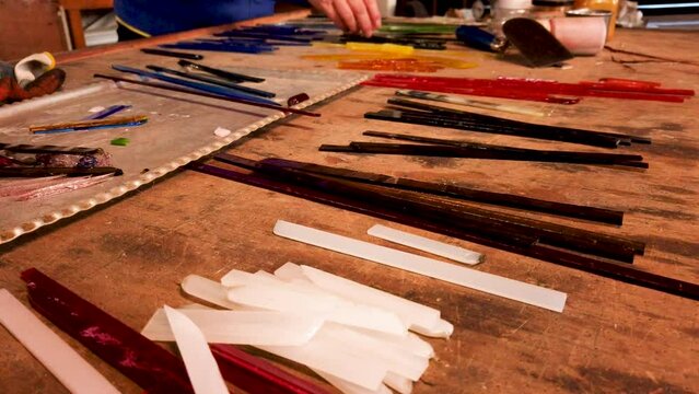  Hands of glass artist arranging colored glass pieces on table in workshop