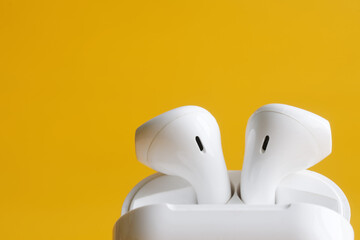 White wireless tws headphones in white charging case on yellow background. Photo. Selective focus....