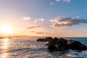 beautiful coast beach with sea gulf water during sunset or sunrise with golden sand, nice black rocks and stones, colorful vawes and clouds in thr sky