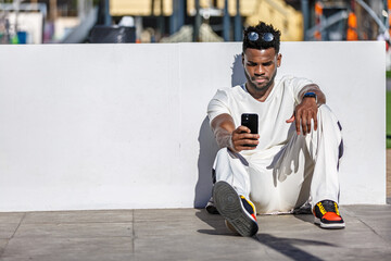 African American Man Sitting on Ground, Looking at Cell Phone
