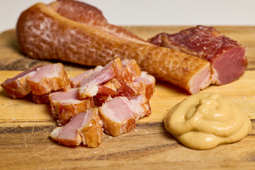 Ham cut into pieces and mustard on a wooden plate.
