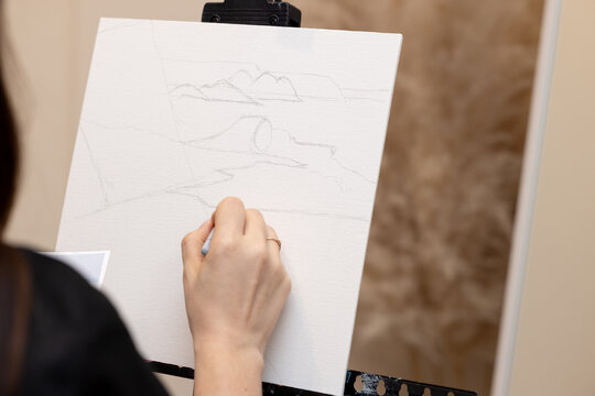 A girl draws a sketch of a future painting on canvas with a pencil. Drawing master class