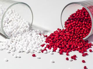 hot cut type red and white masterbatch granules spilled from a shot glass on a white background,...