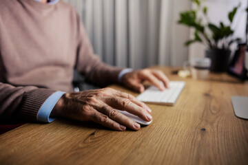 Close up of senior man's hands using computer mouse for work at home office.