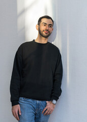 Portrait of a handsome, young man. A smiling Asian guy with a neat beard in a black sweater stands...