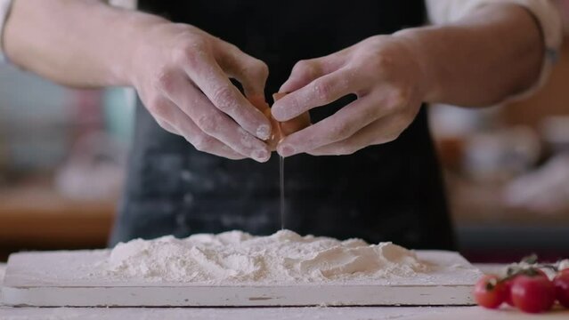Chef is breaking a raw egg and it is falling into a mountain of flour. Concept of the process of cooking dishes from dough or baking. Flour. Food Blog, Flour Products. Bakery products. Preparation of