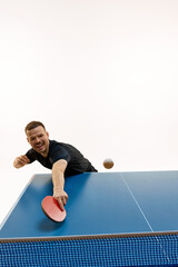 Active table tennis photo shot. Young, fit man, player executing strong return against white studio...
