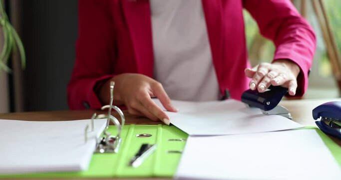 Closeup of hands of manager secretary using hole punch to staple documents in office. Business documentation and archive