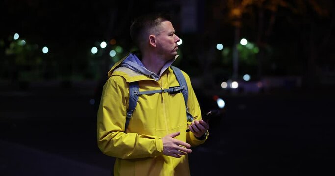 Nervous upset sad guy young man tourist got lost at night in city. Man looks at map navigator on cellular mobile smartphone
