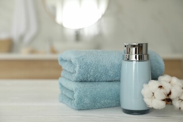 Clean towels, cotton flowers and soap dispenser on white wooden table in bathroom