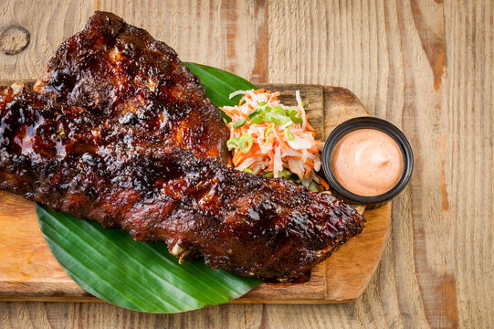 Close up of BBQ spare ribs with coleslaw and sauce on wooden table