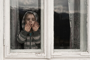 Little grimy boy looking through a dirty old window. He presses his palms against the glass