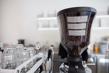 dark roast coffee beans in bean hopper, part of coffee grinder machine in a coffee shop.