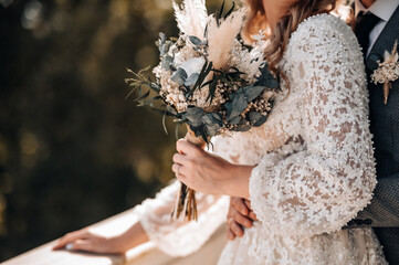 wedding bouquet in boho style collected from wild flowers, the bride holds a bouquet in her hand, in nature, white dress, live plants, a composition of dried flowers