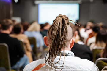 Man with layered, long, trendy hair in a T-shirt, in a crowd at a conference on fashion design and...