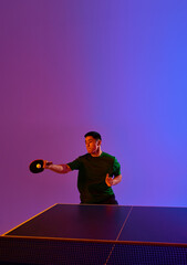 Action shot of Asian man, table tennis player in dynamic pose against gradient blue-purple...