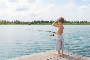 Boy fisherman catches fish in the lake. The child is standing on a wooden pier. Sunny