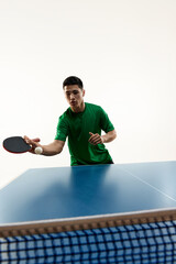 Asian sportsman playing table tennis, eyeing ball for precise hit and make goal in motion against white background. Concept of sport, hobby, lifestyle, match, victory, championship. Ad