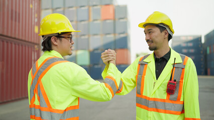 Two asian engineer or foreman shaking hand after working checking at container cargo harbor to loading containers. Two workers shaking hands for success working at container cargo harbor. Teamwork