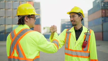 Two asian engineer or foreman shaking hand after working checking at container cargo harbor to loading containers. Two workers shaking hands for success working at container cargo harbor. Teamwork