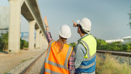 Fototapeta premium Back view of two engineers in safety uniform and helmet discussion and inspection construction process railway. Two engineer working on railway together. Teamwork concept