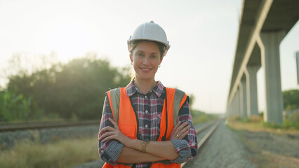 Beautiful engineer woman in safety uniform and helmet standing with arms crossed on railroad...